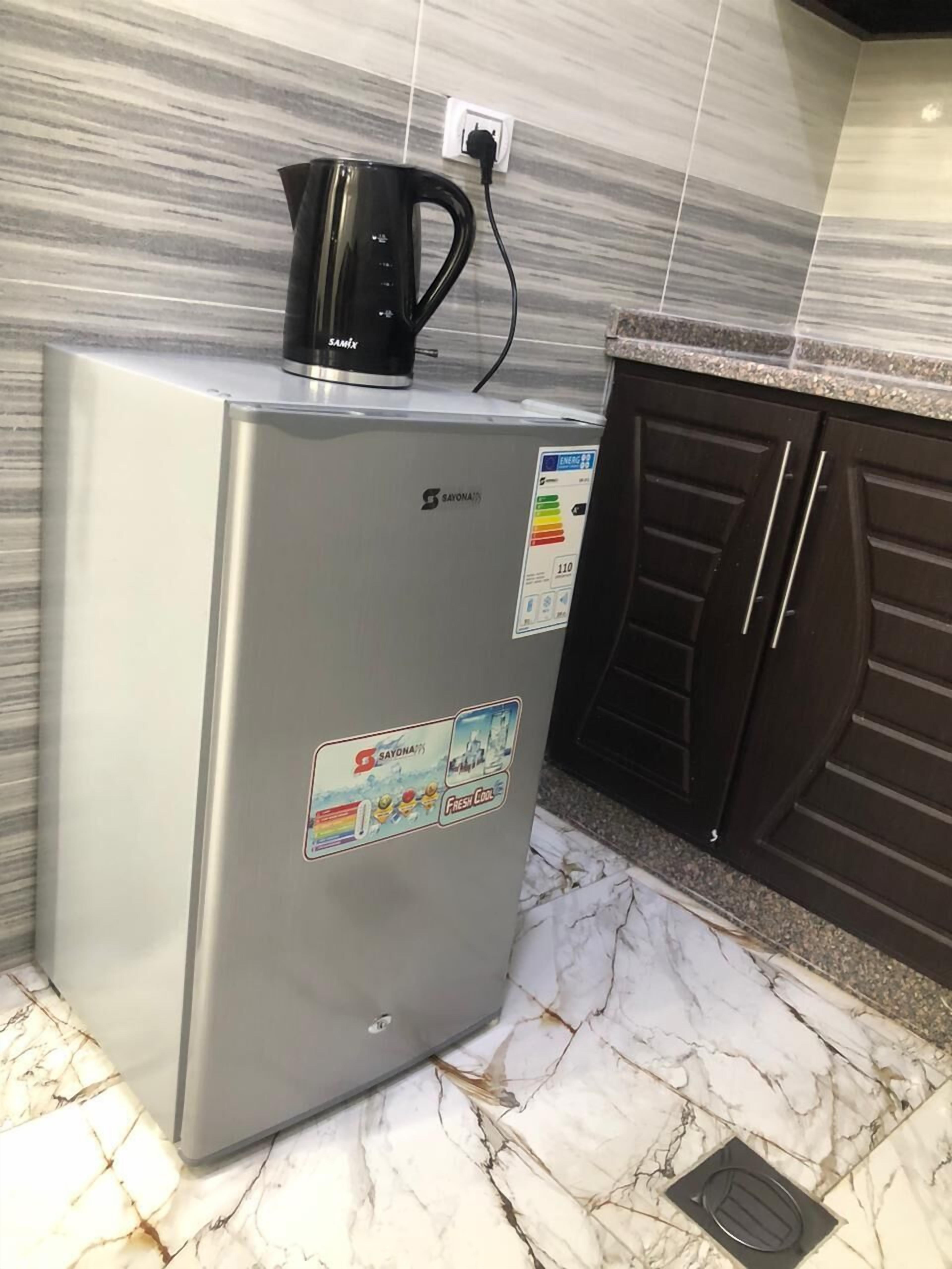 A stainless steel refrigerator with a black kettle on top, a sticker indicating energy efficiency, and a water dispenser.