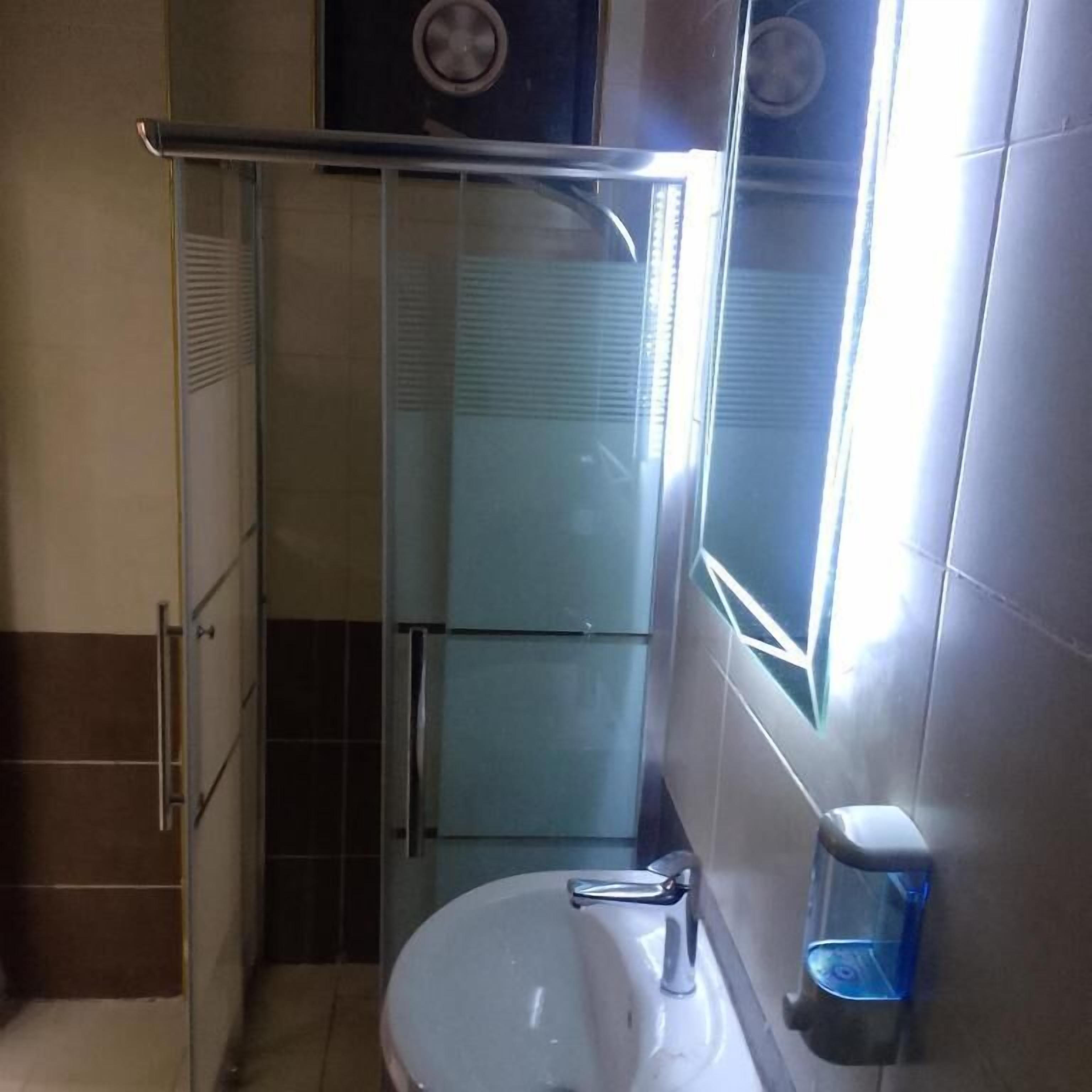 Ein Badezimmer mit einer Duschkabine aus Glas, einem Waschbecken mit chromfarbenen Wasserhahn und einem Seifenspender an der Wand.