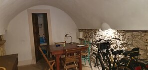 A dining area with a wooden table and chairs, a stone wall, and a bicycle. - Single-family home with a large furnished patio; pets allowed (Bosa)