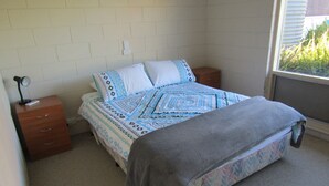 Un dormitorio con cama, mesita de noche, cómoda y ventana.