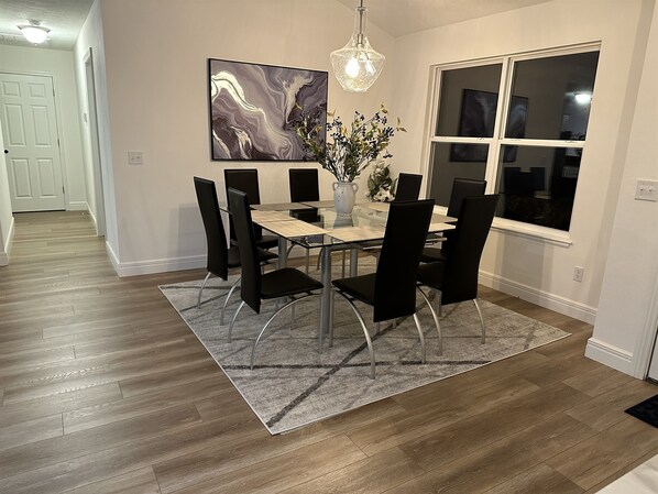 Un coin repas avec une table rectangulaire, des chaises noires, un tapis gris, un vase de fleurs et un grand tableau abstrait accroché au mur.