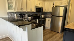 A kitchen with white cabinetry, a stainless steel refrigerator, a microwave, and a black countertop.