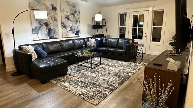 A living room with a black leather sectional sofa, a coffee table, and a patterned rug.