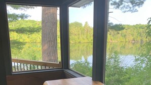 A room with a wooden table and two stools, large windows with a view of a lake and trees. - Totally private boat access cottage with all amenities (Plevna)