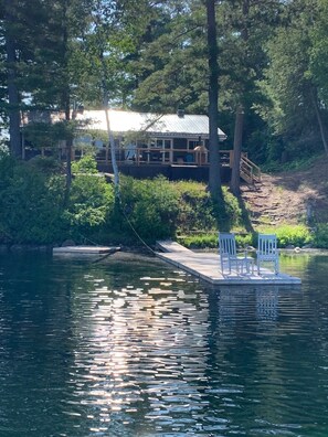 Un chalet au bord du lac, doté d’un quai s’avançant dans l’eau, et entouré d’une forêt dense.
