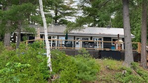 A rustic cabin surrounded by dense forest, with a covered deck and large windows. - Totally private boat access cottage with all amenities (Plevna)