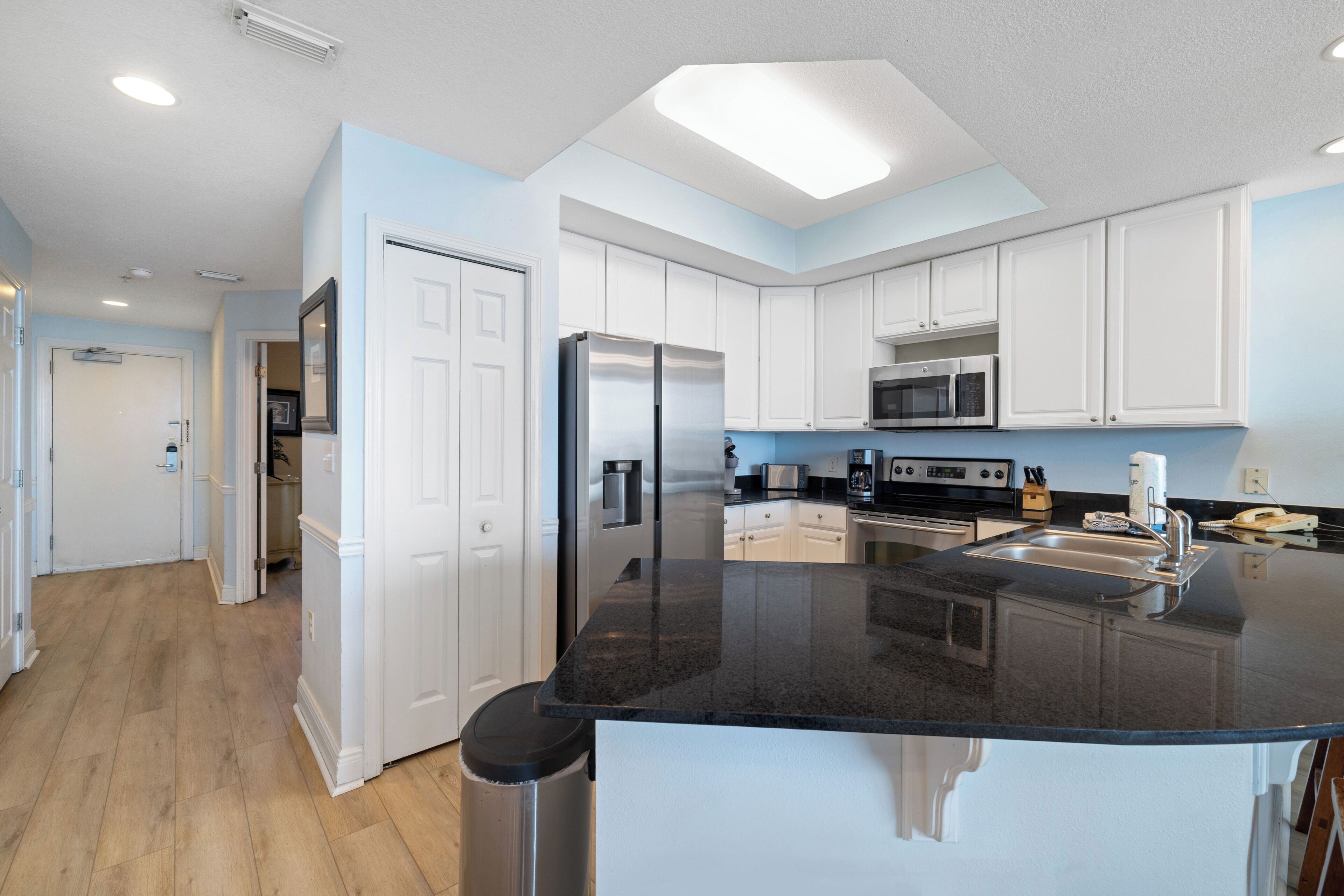 A modern kitchen with white cabinets, a black countertop, stainless steel appliances, and a wooden floor.