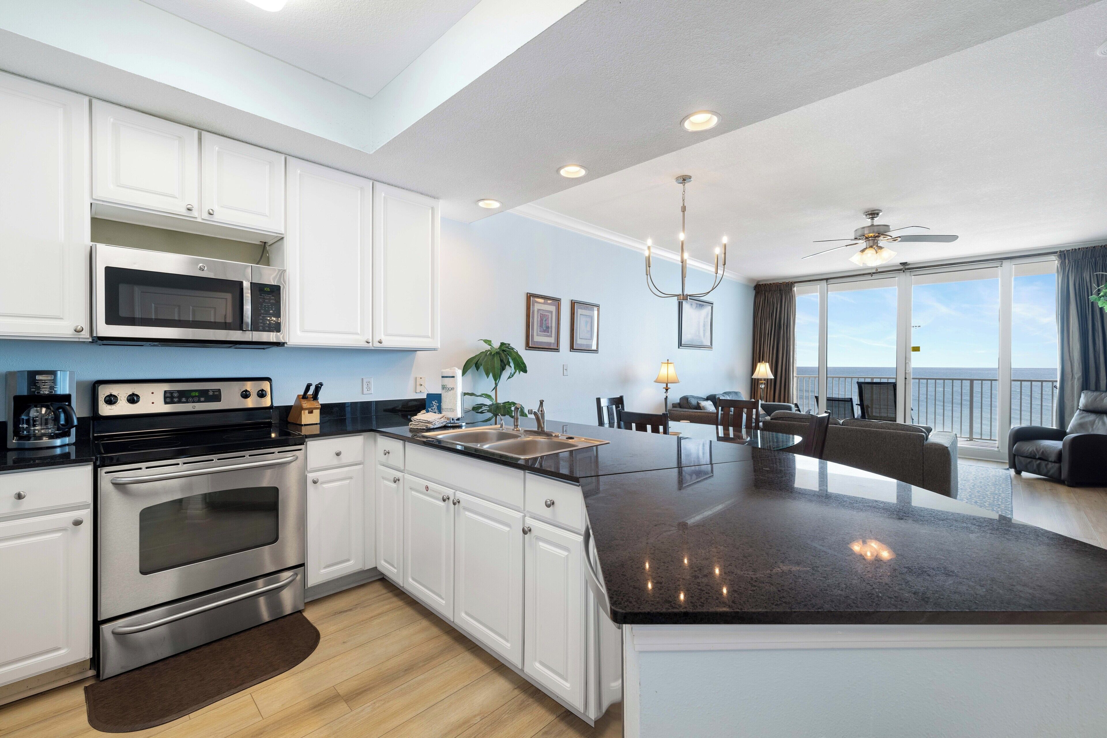 A modern kitchen with white cabinets, a stainless steel oven, a black countertop, and a large island.