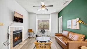 A living room with a fireplace, a sofa, a dining table, and a ceiling fan. - Cozy BoHo 2bd Apartment | Cedar Park/North Austin (Austin)