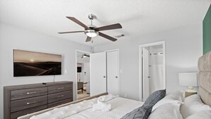 Ein Schlafzimmer mit einem Bett, einem Schminktisch, einem Deckenventilator, einem Fernseher und einer Tür zu einem Badezimmer.