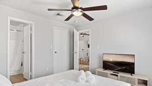 Ein Schlafzimmer mit einem Bett, einem Deckenventilator, einem Fernseher und einem Spiegel.