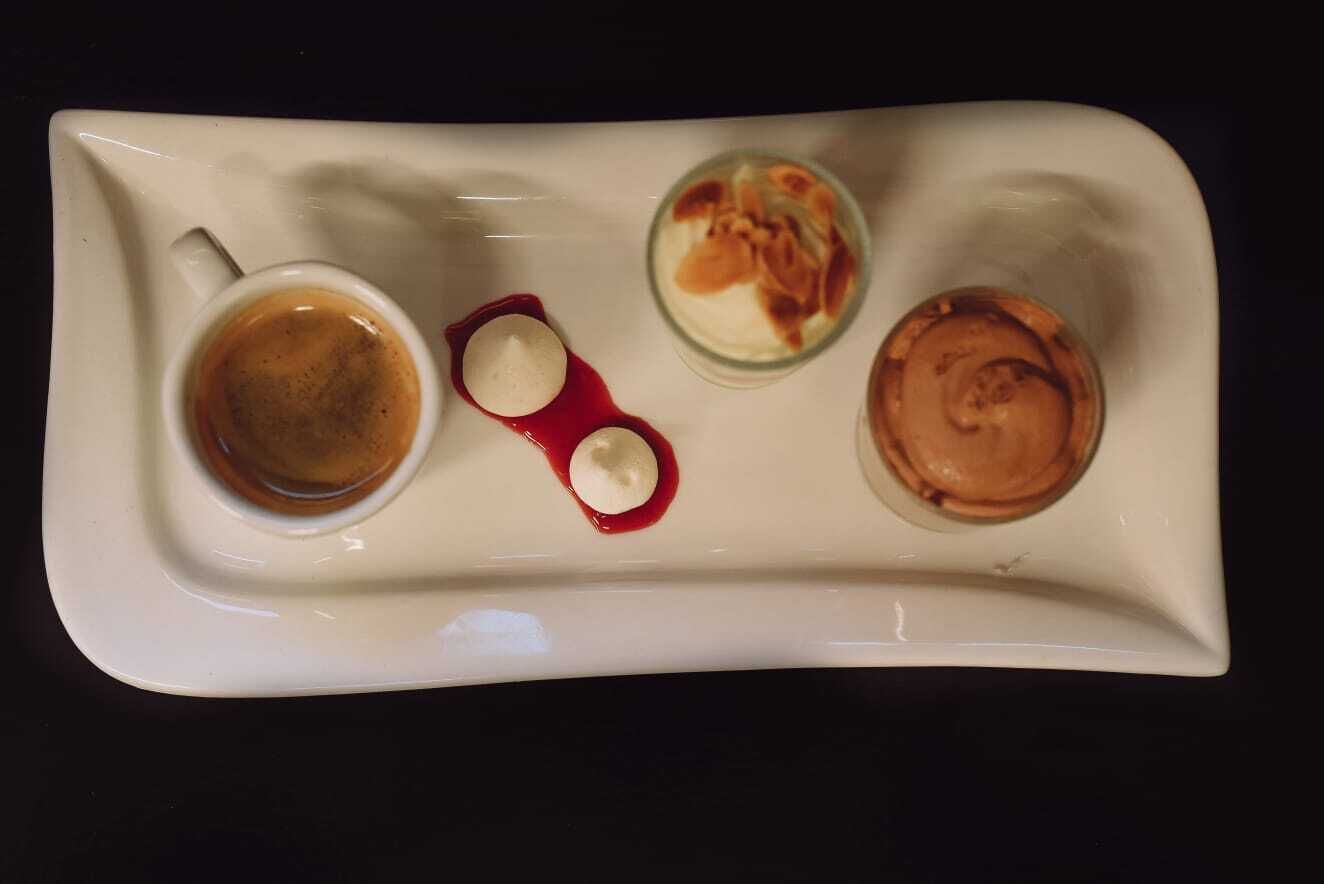 A white tray with a cup of coffee, a dessert with whipped cream and a red sauce, and a glass of a creamy beverage.