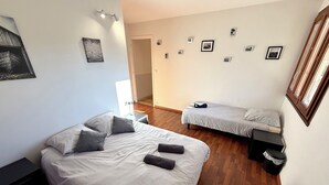 Une chambre avec deux lits, un plancher en bois, une porte et un mur orné de tableaux encadrés.