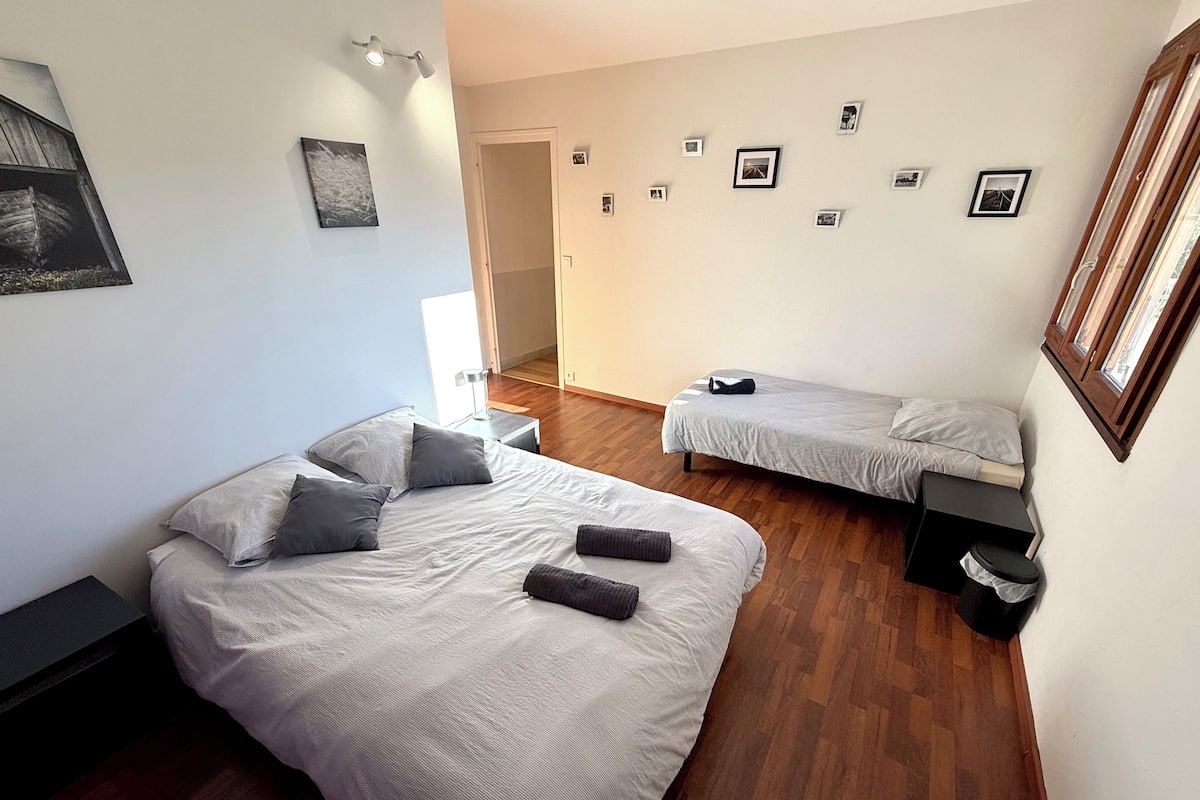 Un dormitorio con dos camas, piso de madera, una puerta y una pared decorada con marcos.