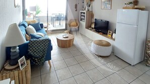 Una sala de estar moderna con un sofá, una mesa de centro, un reposapiés, un televisor y un refrigerador.