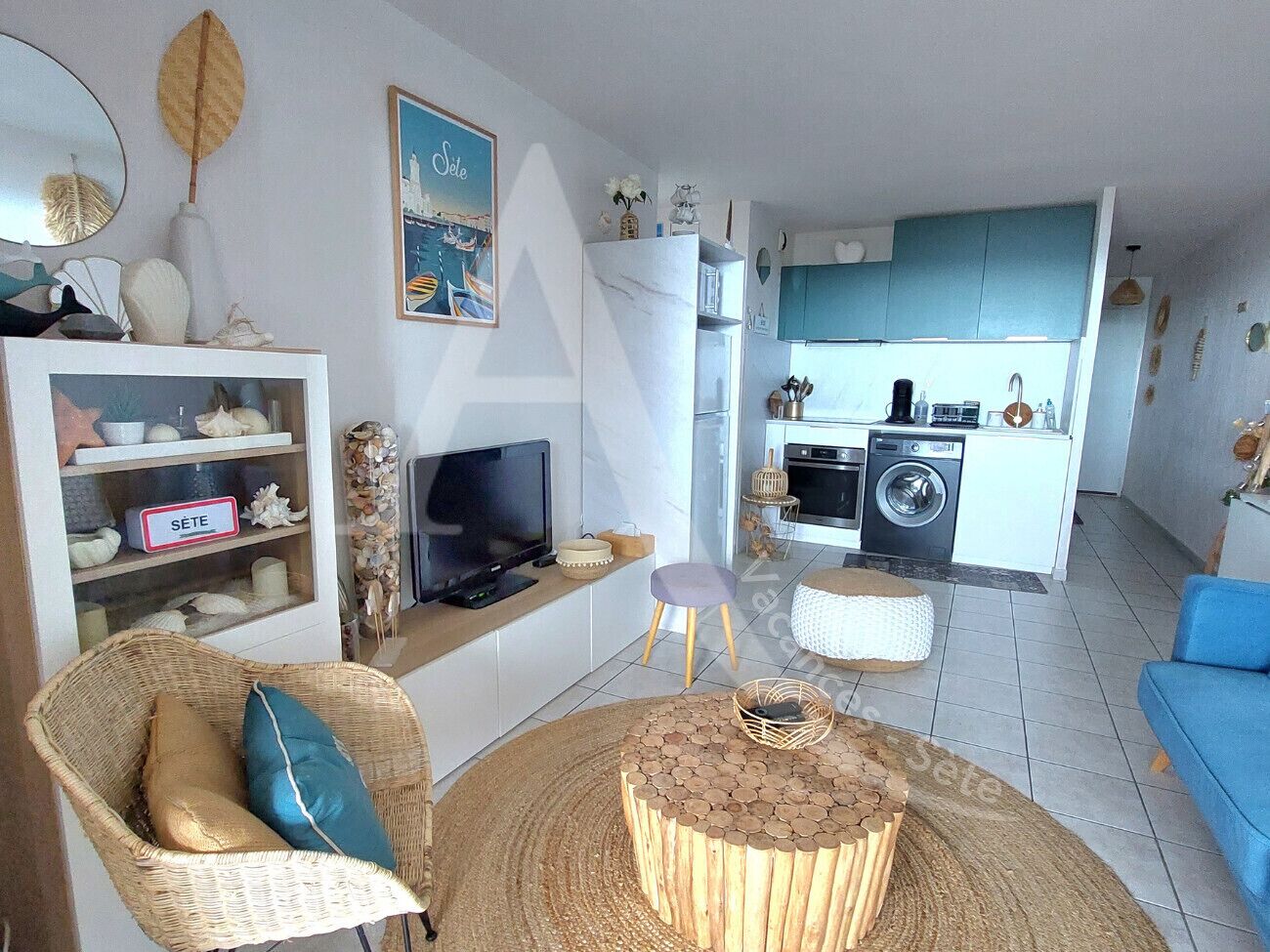 Un salon moderne avec un téléviseur, des meubles en osier et une cuisine en arrière-plan.
