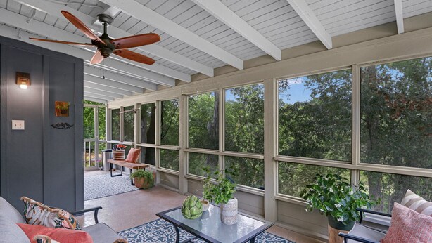 A sunroom with a ceiling fan, large windows, a glass coffee table, and a sofa with patterned cushions. - Lily Pad I Wimberley cottage on Cypress Creek! (Wimberley)