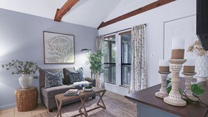 A cozy living room with a grey sofa, a woven coffee table, and a large plant. - Lily Pad I Wimberley cottage on Cypress Creek! (Wimberley)