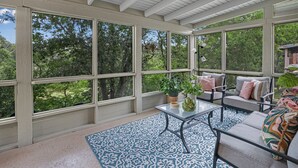 A sunroom with large windows, a patterned rug, and outdoor furniture. - Lily Pad I Wimberley cottage on Cypress Creek! (Wimberley)