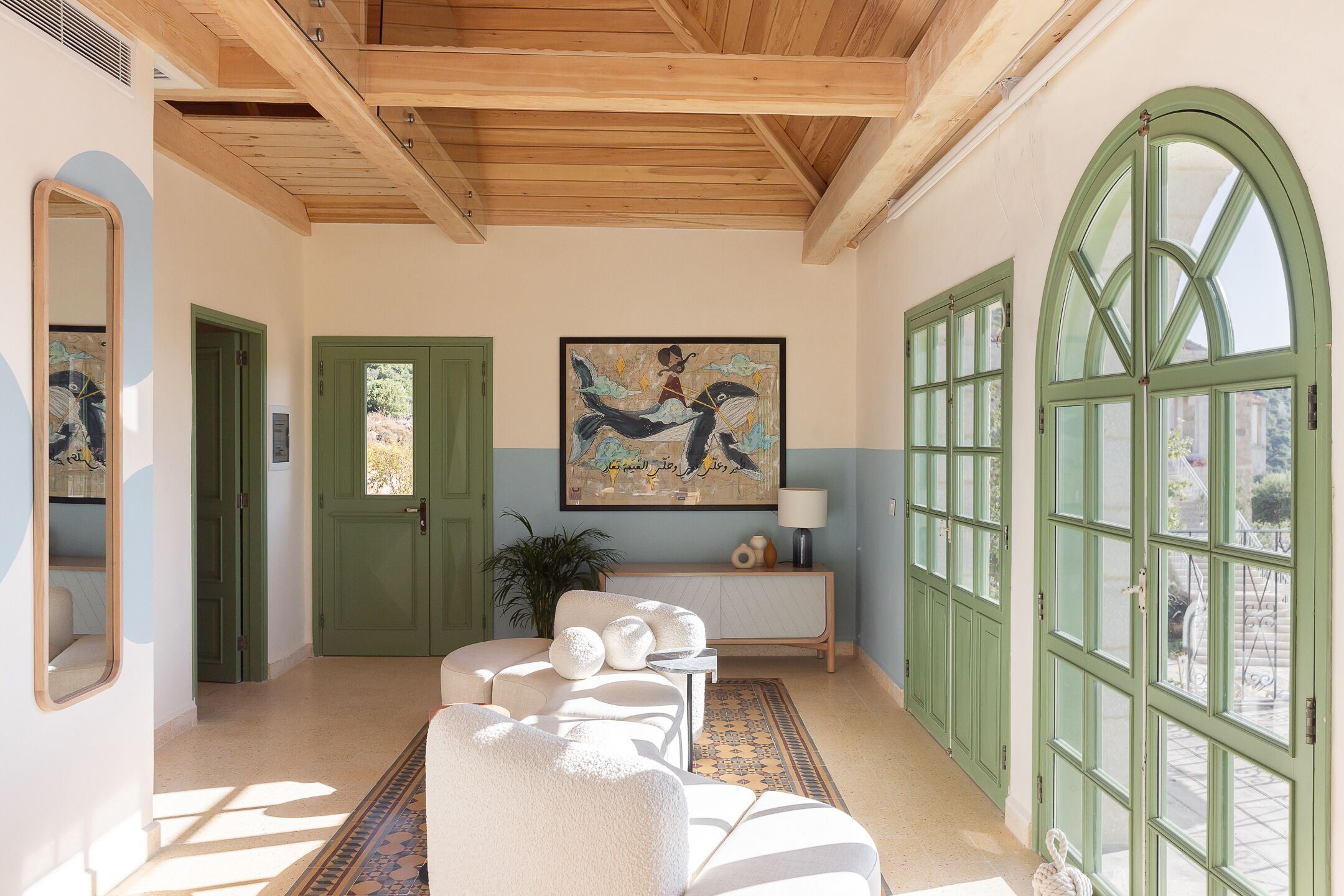 A spacious living area with a high ceiling, green doors, and a large window.