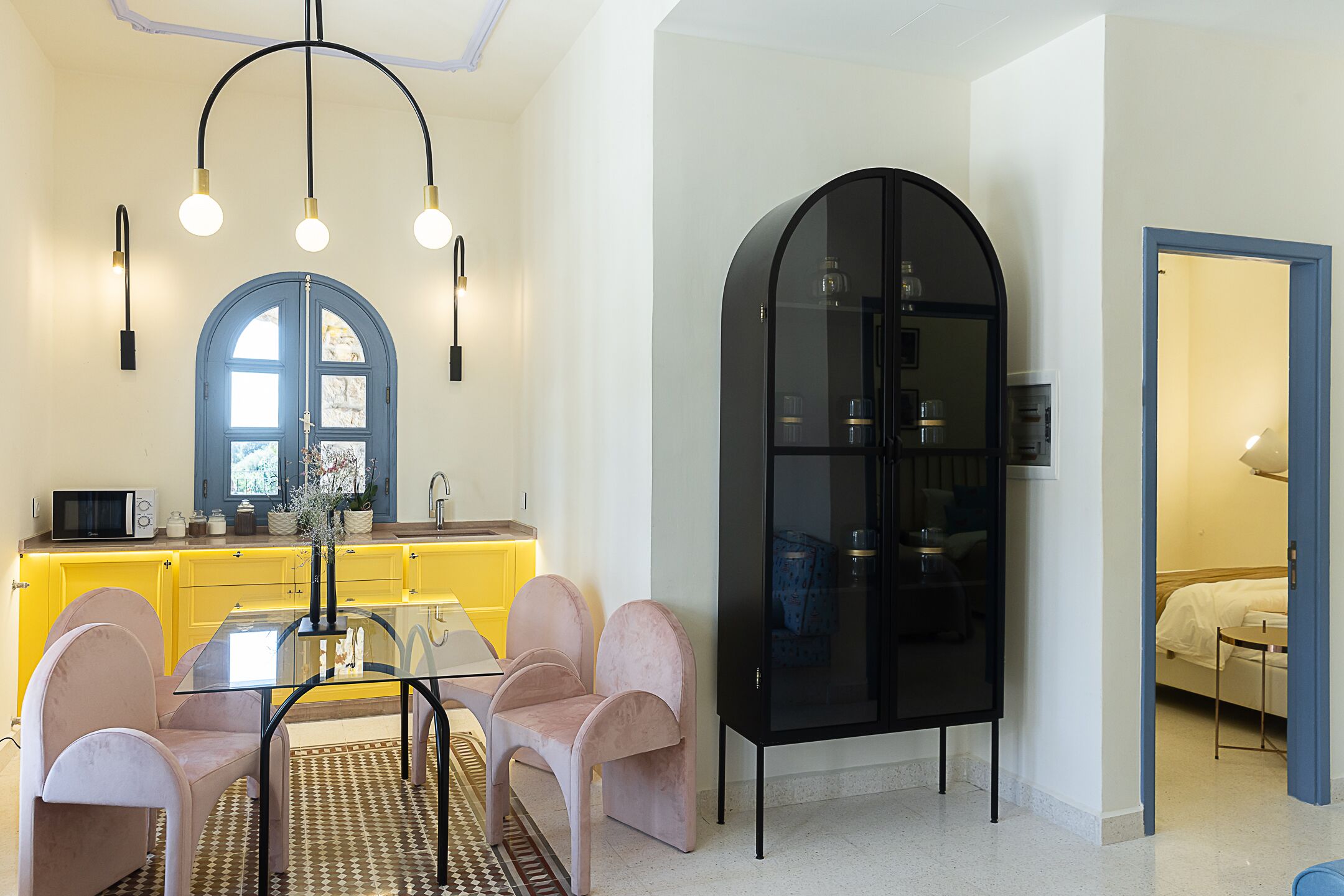 A modern kitchen with yellow cabinets, a glass dining table, and pink chairs.