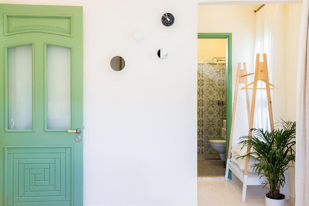 A green door with a mirror and three clocks on the wall.