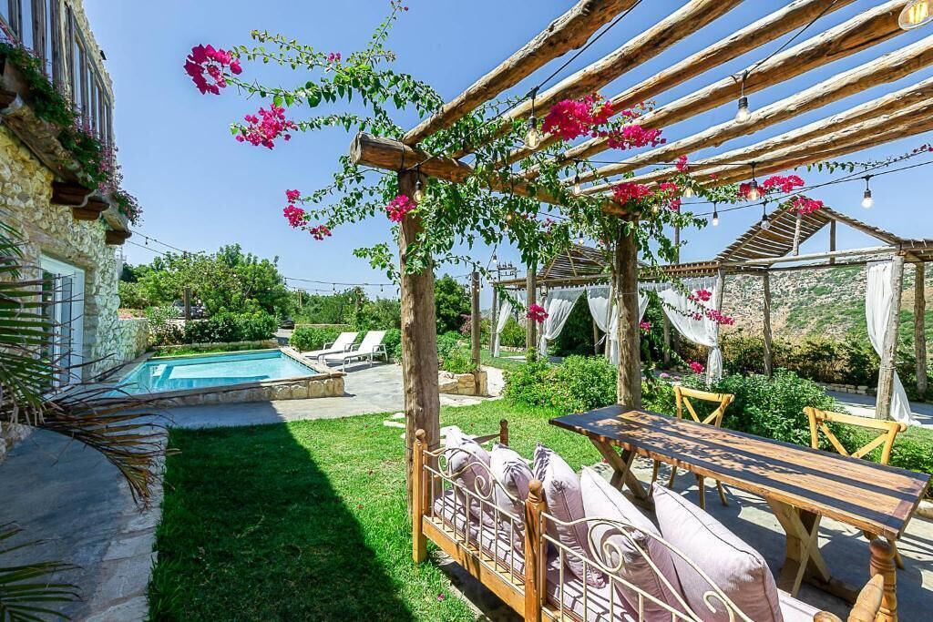 A garden with a wooden pergola, a pool, and a dining area with a table and chairs.