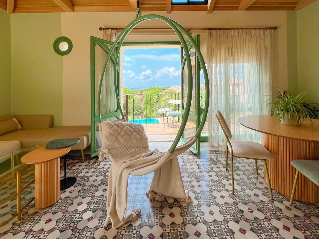 A room with a green-framed window, a hanging chair, a sofa, a small table, and a potted plant.