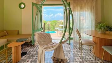 A room with a green-framed window, a hanging chair, a sofa, a small table, and a potted plant.