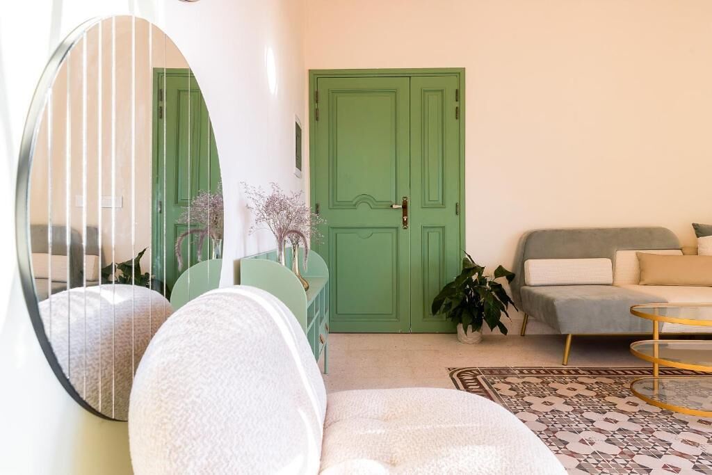 A living room with a green door, a round mirror, a sofa, a coffee table, and a patterned rug.