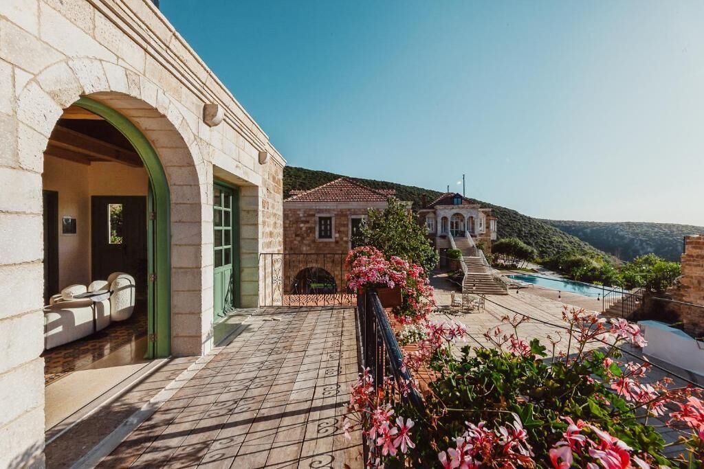 A stone building with an arched entrance, a pool area with steps, and a hillside backdrop.