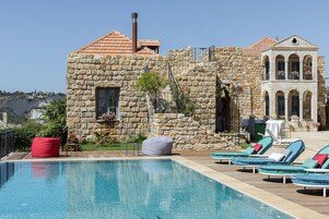 Un bâtiment en pierre doté d’une piscine et de chaises longues.