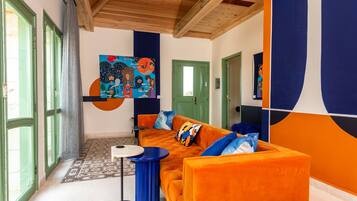 A modern living room with a large orange sofa, a round coffee table, and a colorful abstract painting on the wall.