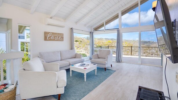 A spacious living room with a white ceiling, large windows, a white sofa, a white armchair, and a coffee table. - Stunning Home w/Ocean-Mountain Views in East Oahu Serene Family Vacation (Honolulu)