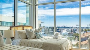 A modern hotel room with large windows offering a city view, a bed with a headboard, and a bedside table with a lamp. - @ Marbella Lane - Sleek Corner | Ocean View (Long Beach)