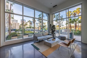 Una habitación amplia con ventanas grandes, un sofá gris, una mesa de centro y dos sillas.