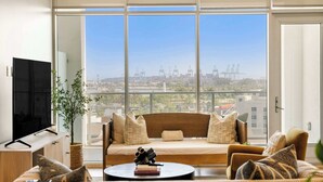 A modern living room with a large window, a flat-screen TV, a sofa, and a coffee table with books and sunglasses. - @ Marbella Lane - Panoramic Delight Dream Escape! (Long Beach)