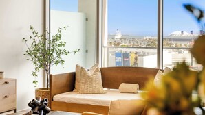 A modern living room with a large window, a wooden sofa, a small side table, and a potted plant. - @ Marbella Lane - Panoramic Delight Dream Escape! (Long Beach)