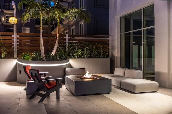 An outdoor seating area with a fire feature, modern furniture, and a palm tree. - @ Marbella Lane - Panoramic Splendid Ocean Views! (Long Beach)