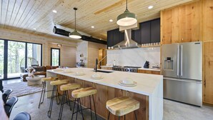 A modern kitchen with a large island, bar stools, stainless steel appliances, and wooden cabinetry.