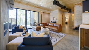 A spacious living room with a fireplace, leather sofas, and a large window offering a view of trees.