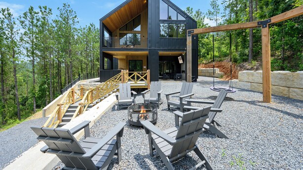 A modern two-story cabin with a deck, outdoor seating, and a fire pit.