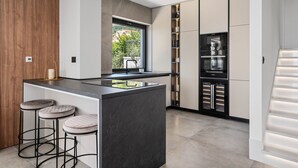 A modern kitchen with a central island, bar stools, a built-in oven, and a refrigerator. - Stylish property with heated 32sqm private pool, 5 bedrooms, 5 bathrooms, 1km from the beach (Podstrana)
