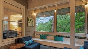 A cozy outdoor seating area with a bench and cushions, a small table, and a view of the outdoors. - Great Second Cottage at Hidden Dunes (Miramar Beach)