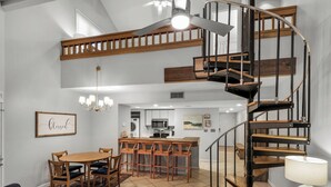 A spacious living area with a dining table, sofas, and a spiral staircase. - Great Second Cottage at Hidden Dunes (Miramar Beach)
