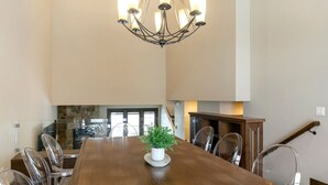 Un vaste espace dédié à la salle à manger, avec une table en bois, des chaises transparentes et un lustre.