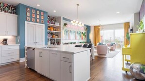 Cocina moderna con armarios blancos, una isla central y un comedor con un detalle amarillo.