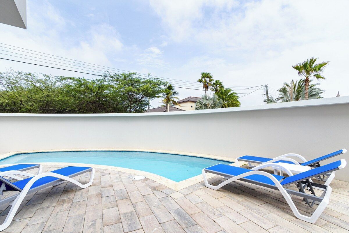 A swimming pool with lounge chairs and a tiled deck.
