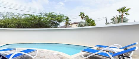 A swimming pool with lounge chairs and a tiled deck.