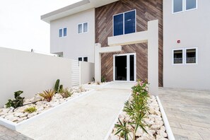 A modern building with a flat roof, a central entrance with a glass door, and a stone pathway leading to the entrance.